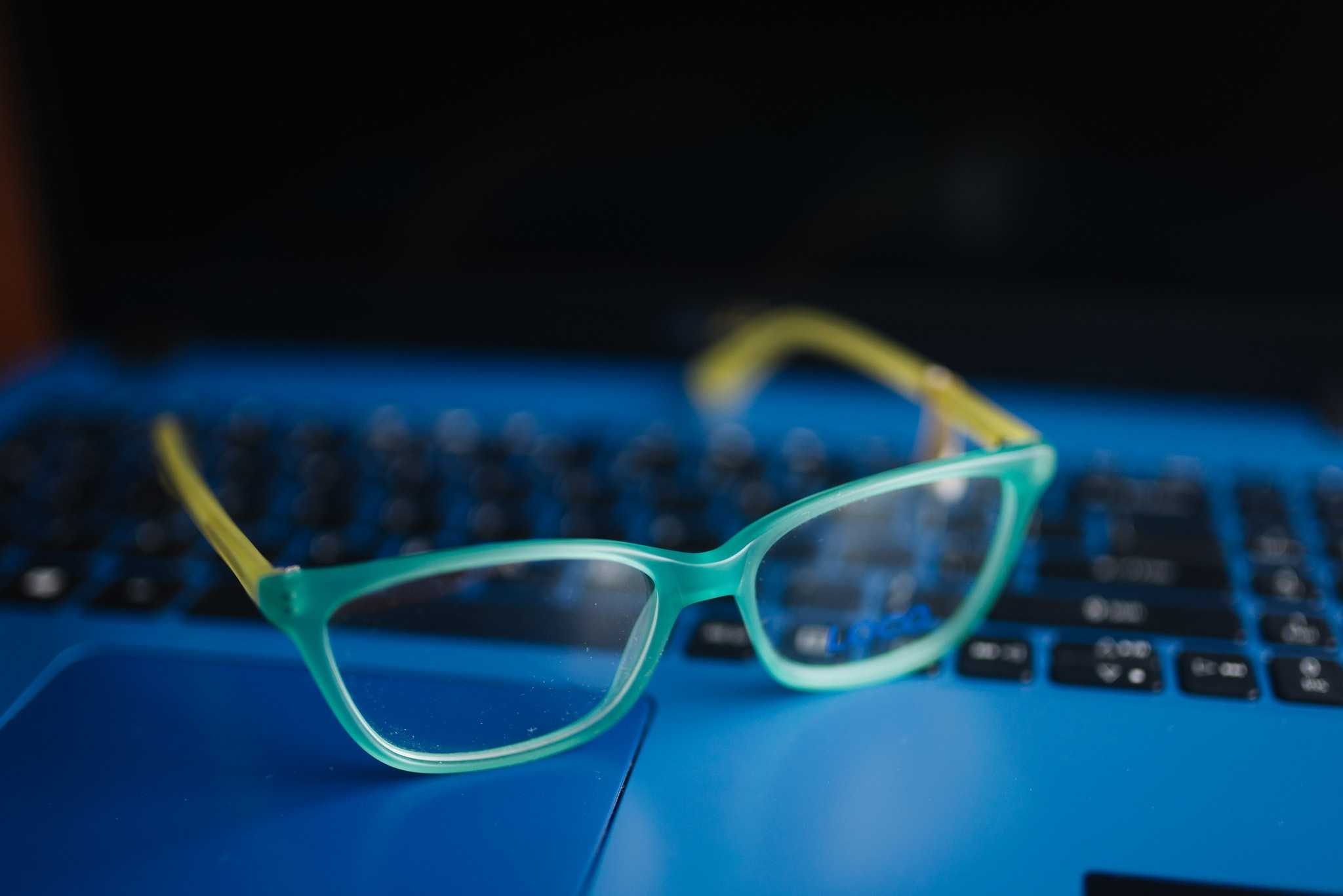 Close-up of the glasses with light blue frame on a blue laptop.